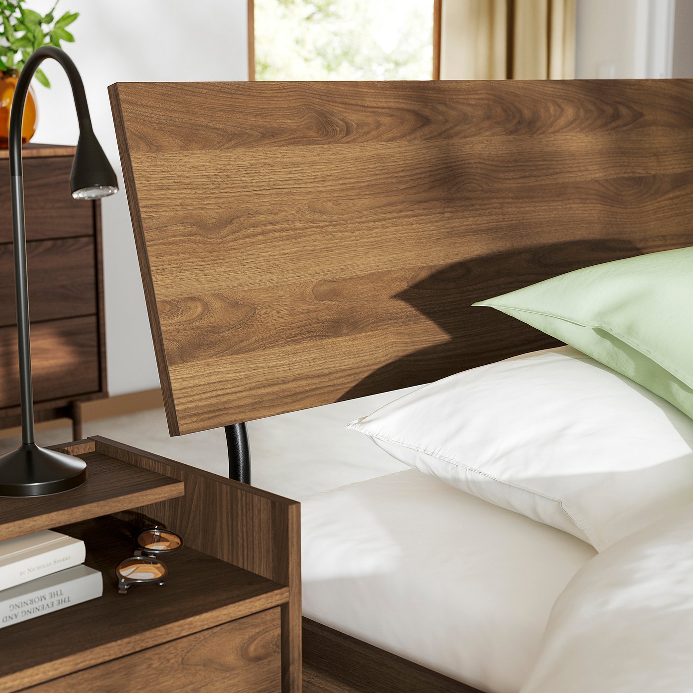 Wooden bed with curved slats and green pillow. Black lamp and books on bedside table.