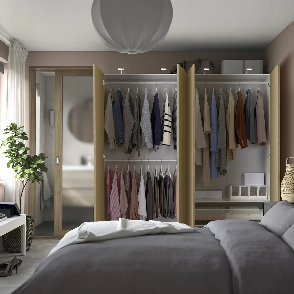 Bedroom with open wardrobe displaying clothes, featuring integrated lighting and adjustable feet.