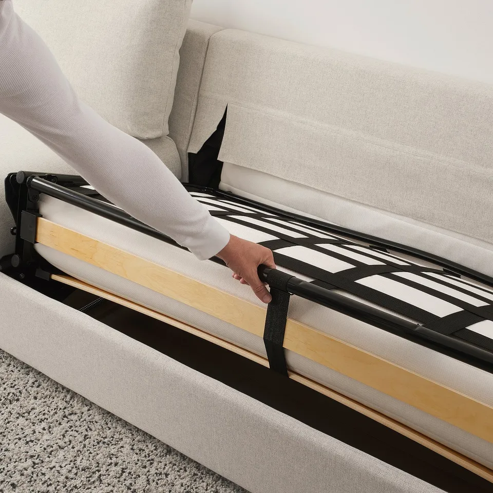 Person adjusting sofa-bed mechanism with wooden slats and black straps for easy conversion into a bed.
