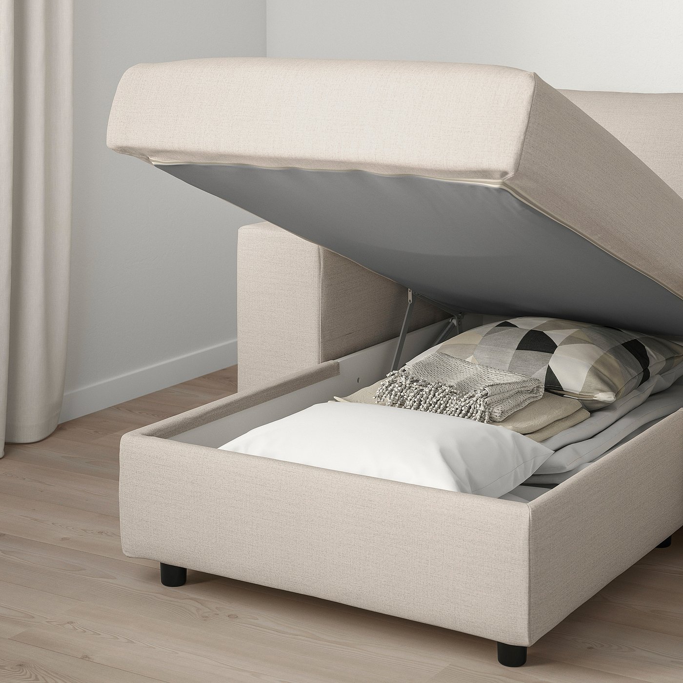 Modern beige sofa with ottoman, open storage with pillows and blankets, ideal for living rooms.