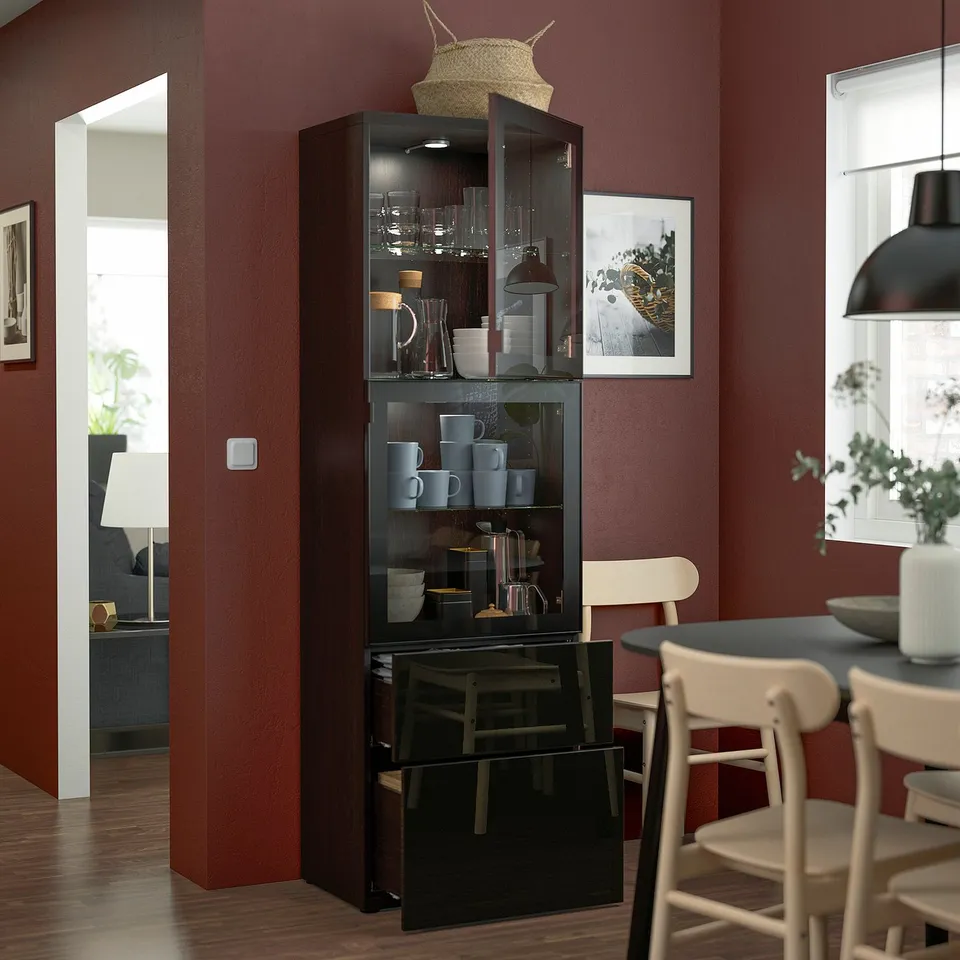 Glass cabinet with shelves, drawers, and basket on red wall in stylish dining room.