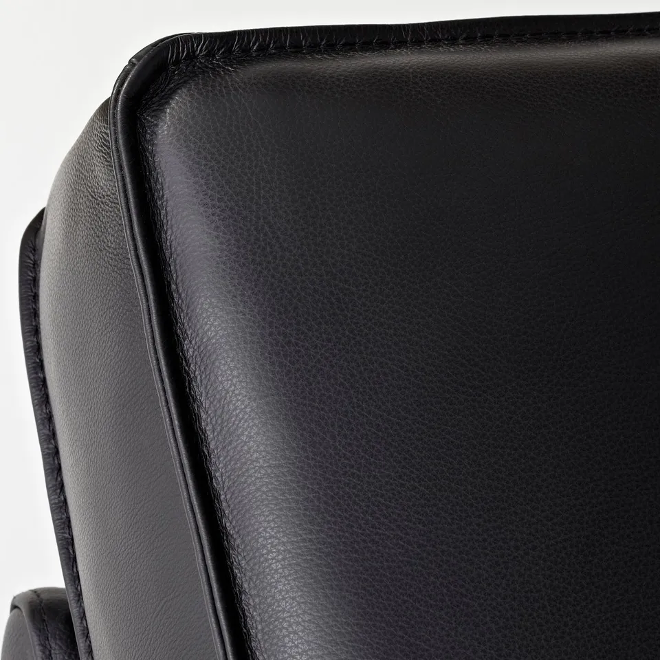 Close-up of black leather sofas corner, showcasing smooth texture and sturdy stitching.