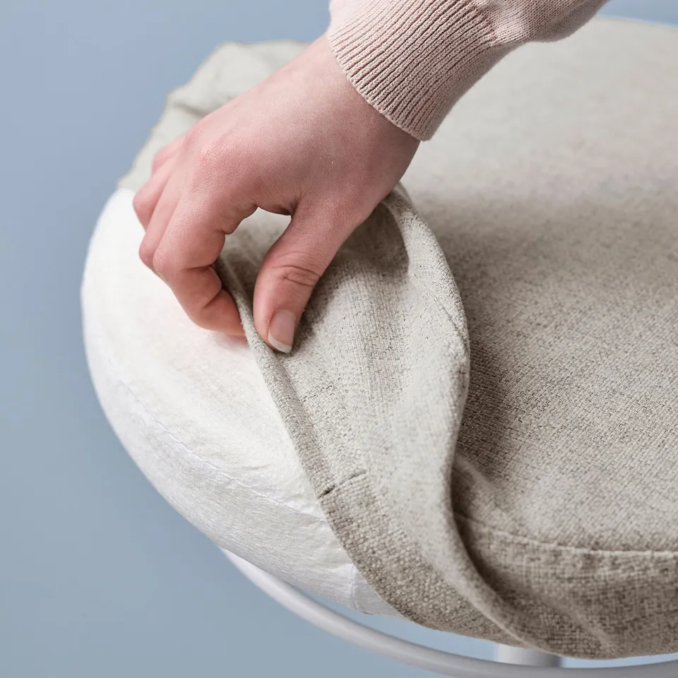 Hand holding LIDKULLEN lid, a sit/stand support, demonstrating its removability for easy cleaning.