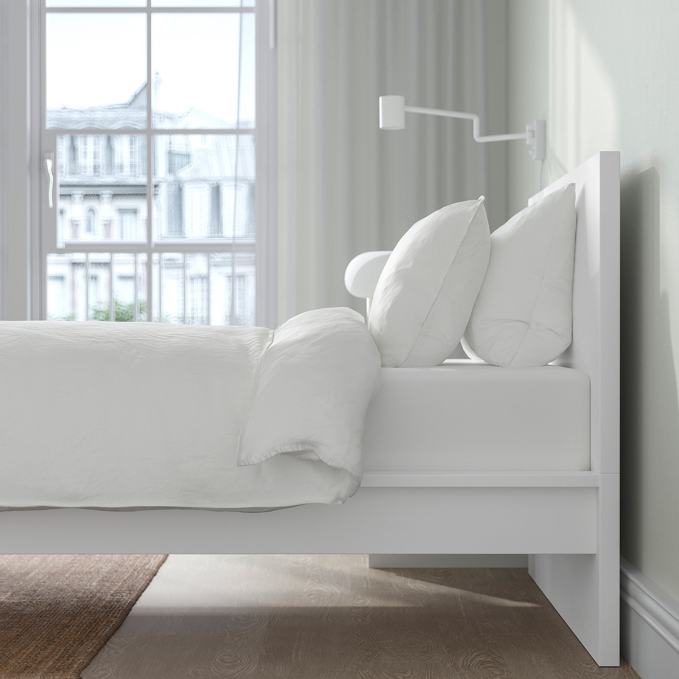 Bed with adjustable sides and high headboard, white, near large window with city view; plush white pillows and blankets, brown patterned rug below.