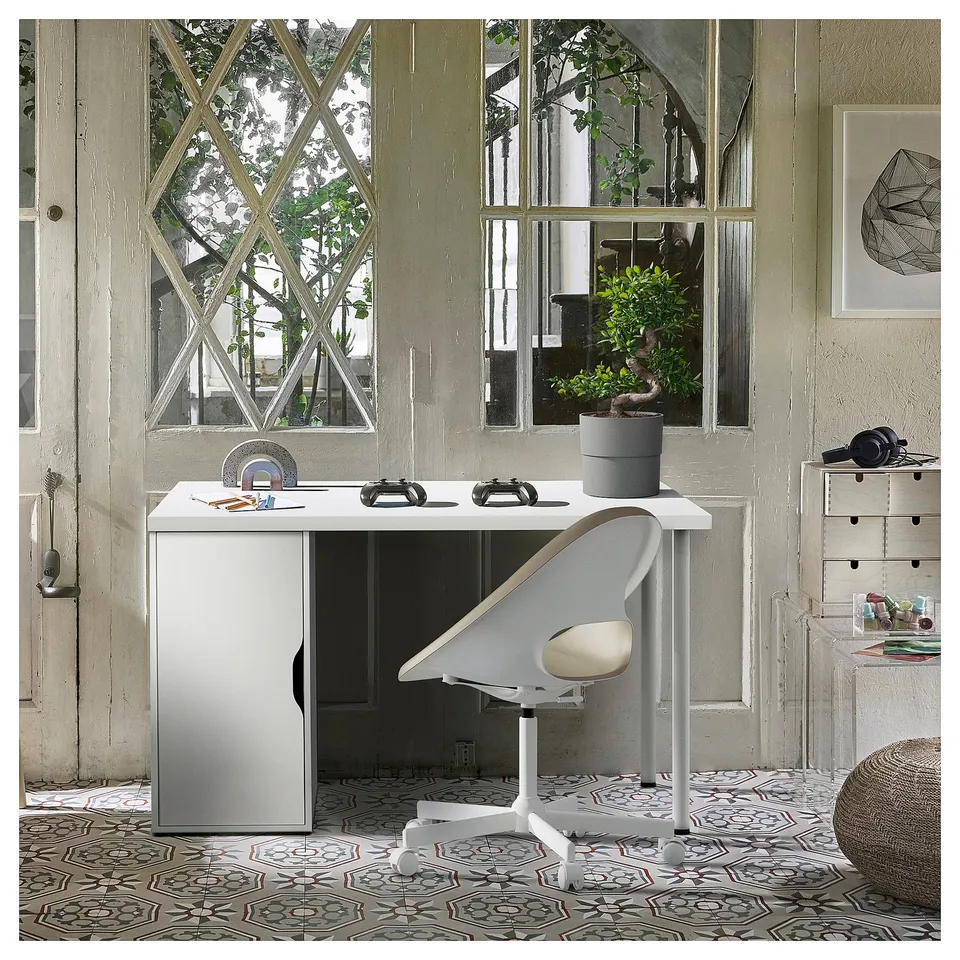A stylish white LAGKAPTEN desk with a door cabinet and a white chair, set against large, patterned windows in a cosy room.