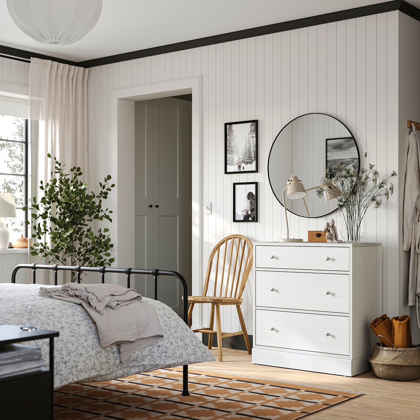 Bedroom with white HAVSTA 3-drawer chest, mirror, plant on colourful rug beside cosy bed.