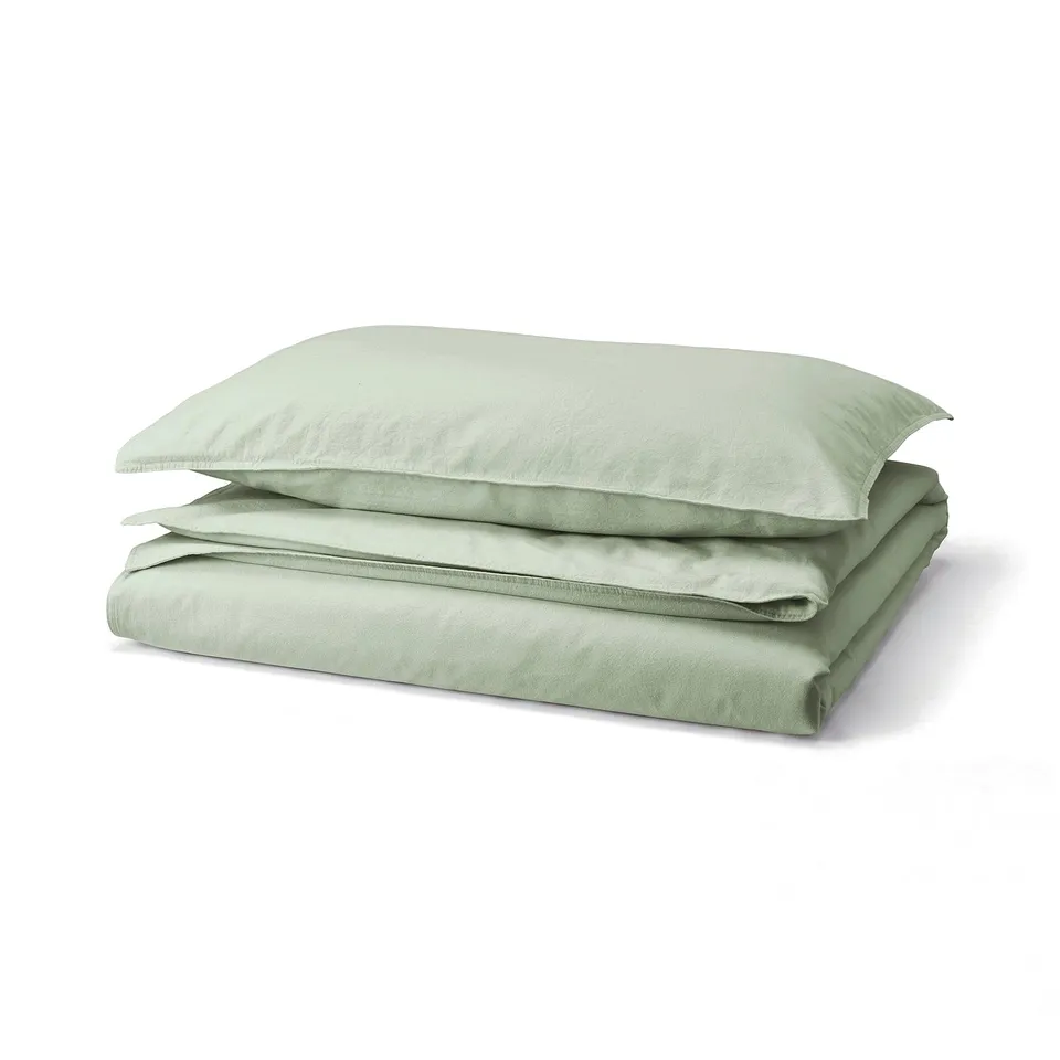 A stack of soft green bedding: two pillows and a folded duvet, all neatly arranged, displaying light green colour and smooth cotton texture.