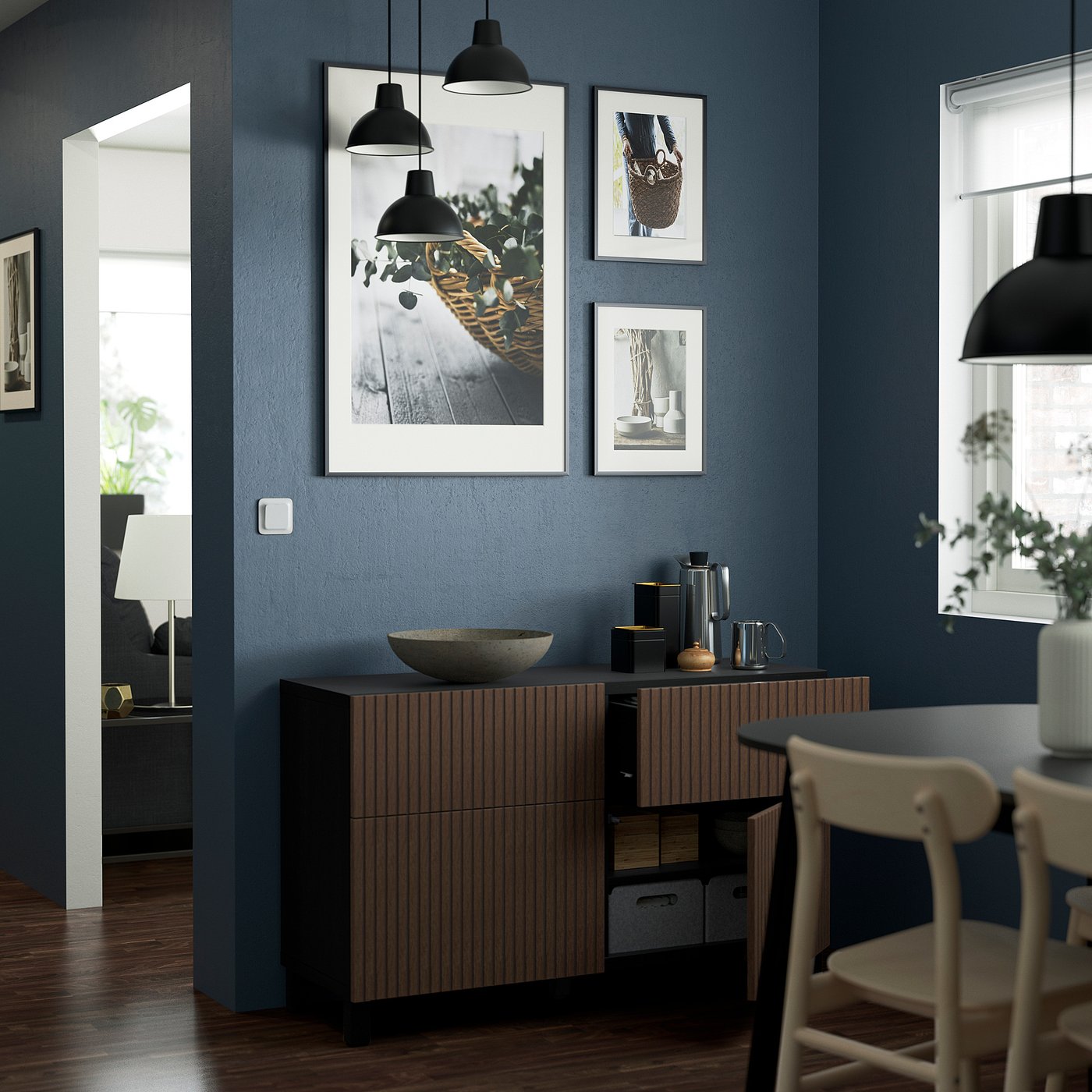 Modern kitchen with dark blue walls, wooden sideboard, hanging lights, and framed art above.