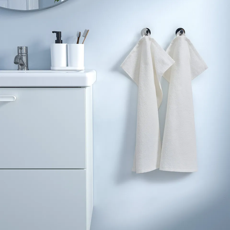 A white LUDDVIAL towel hung on hooks next to a bathroom vanity. The towel is rectangular, made of cotton, and appears smaller than the vanity.