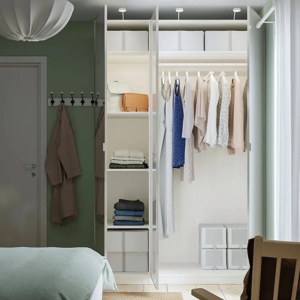 Modern bedroom with PAX closet; hanging clothes, folded sweaters, and towels, plus storage bins.