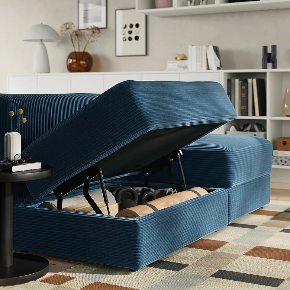 Blue corduroy sofa with storage. Seat raised, revealing blankets and pillows.