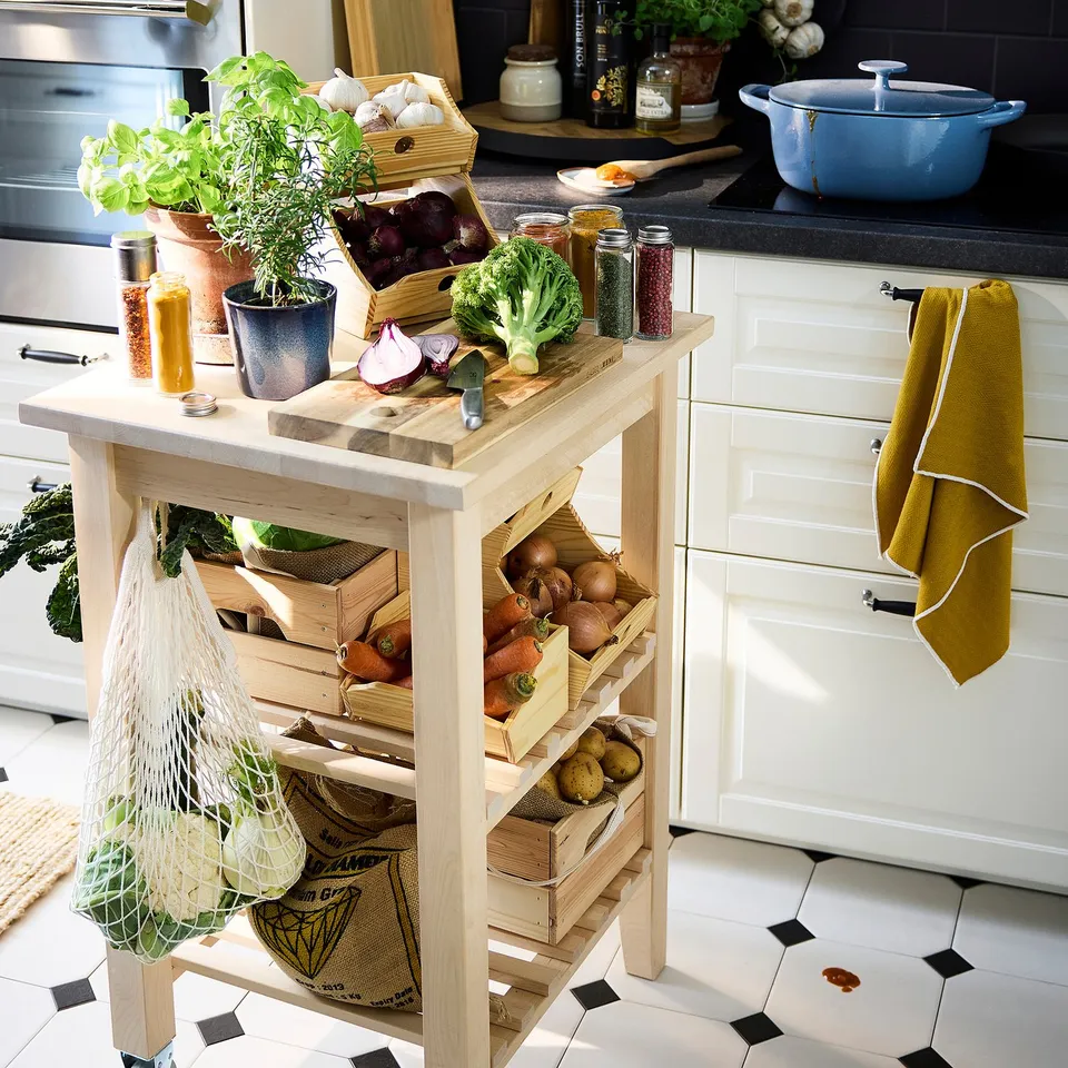 Wooden kitchen organiser with crates of vegetables and herbs, potted plants, and kitchen items on counter.
