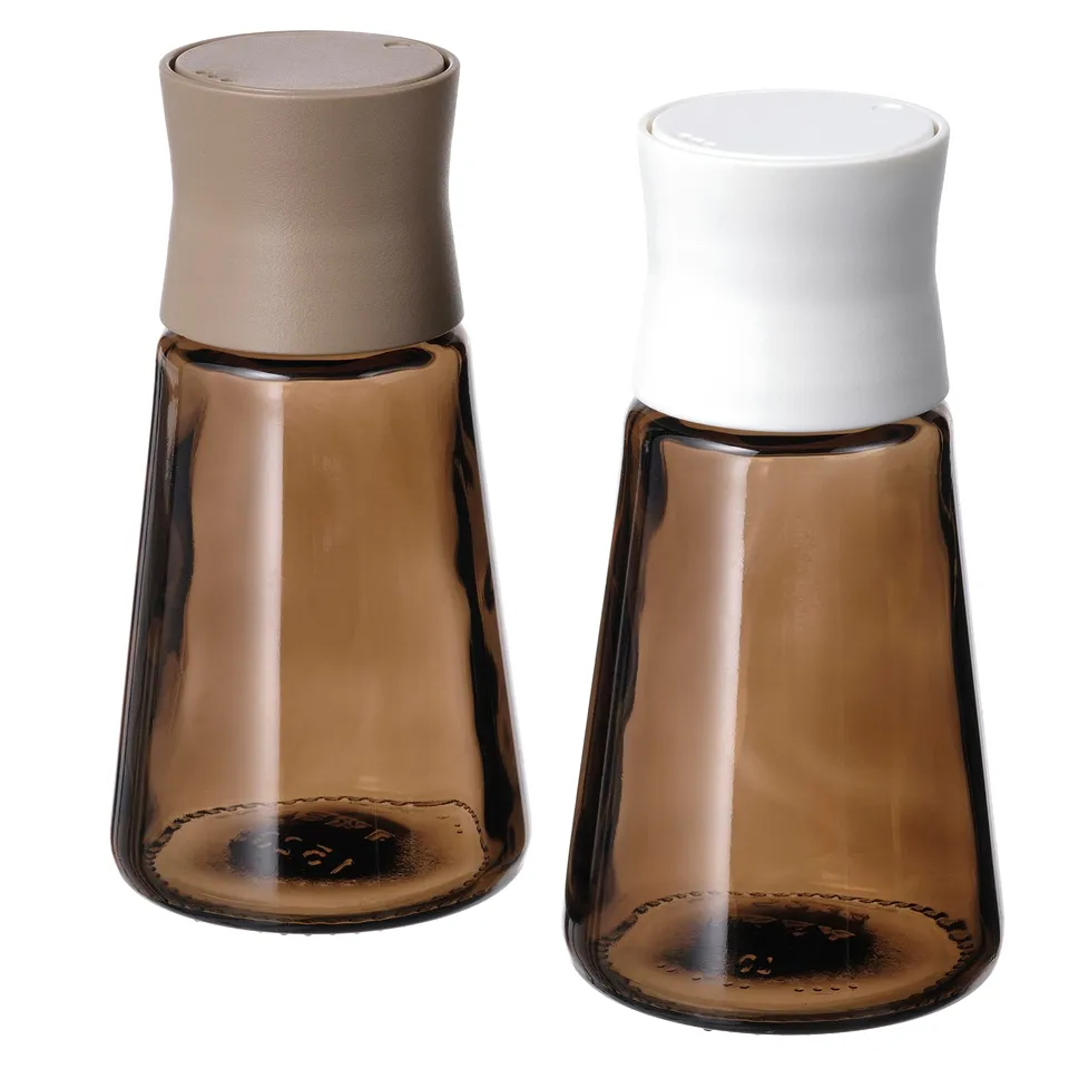 Two HALVTOM glass spice jars, one with beige cap, one with white. Sleek, tapered design.