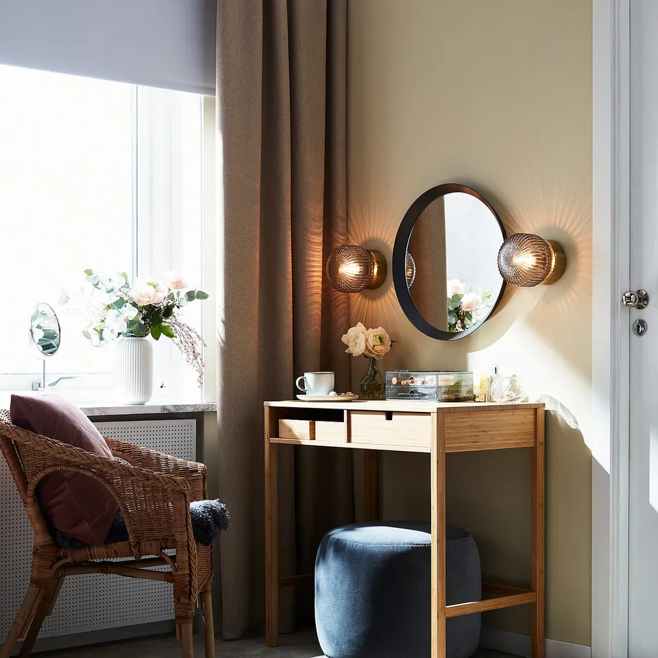 Luxurious bedroom with wicker chair, maroon pillows, vanity, round mirror, and SOLKLINT lamps.