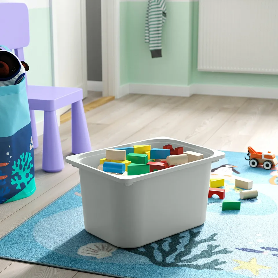 Bin filled with colourful blocks, surrounded by toys on a beach-themed rug in a childs playroom.