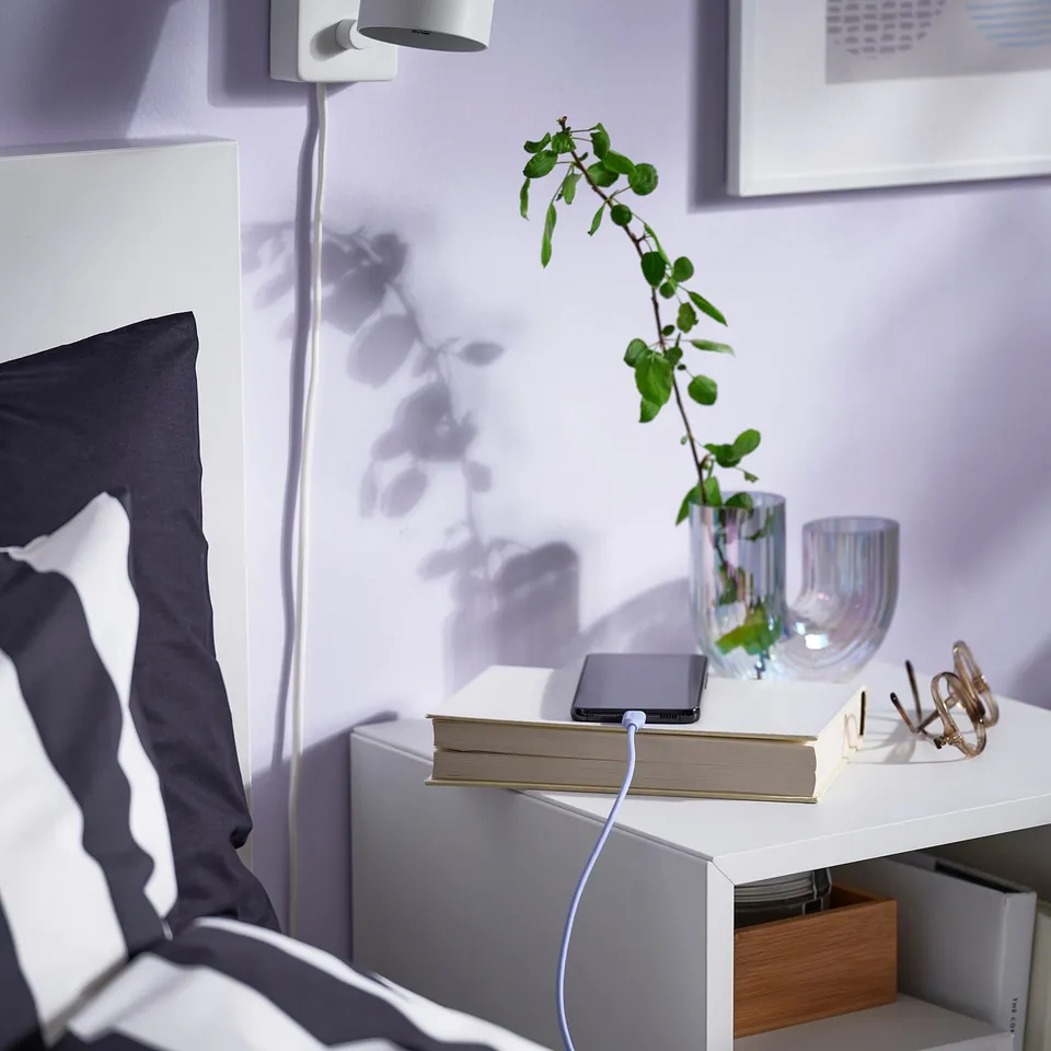 A charging cable on a bedside table connects to a phone atop a book, showcasing its flexible design and overheating protection.
