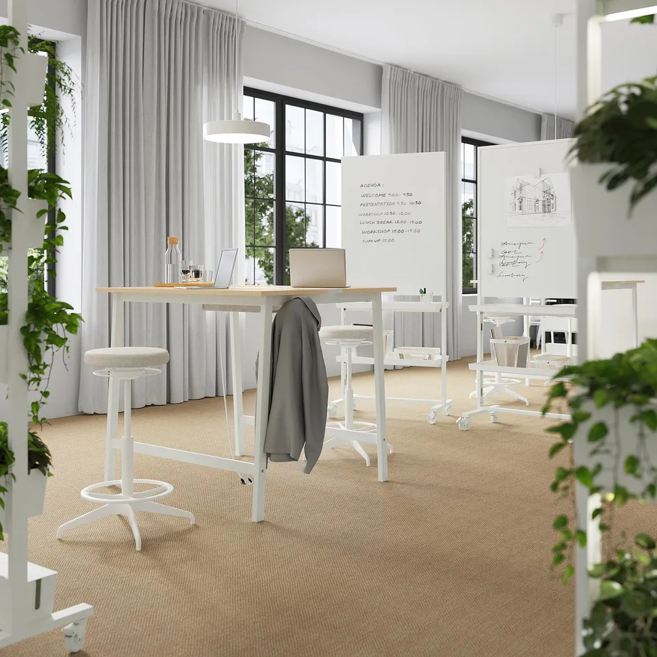 Modern office with MITTZON tables, stools, large windows, whiteboards, and plants for a bright, productive space.