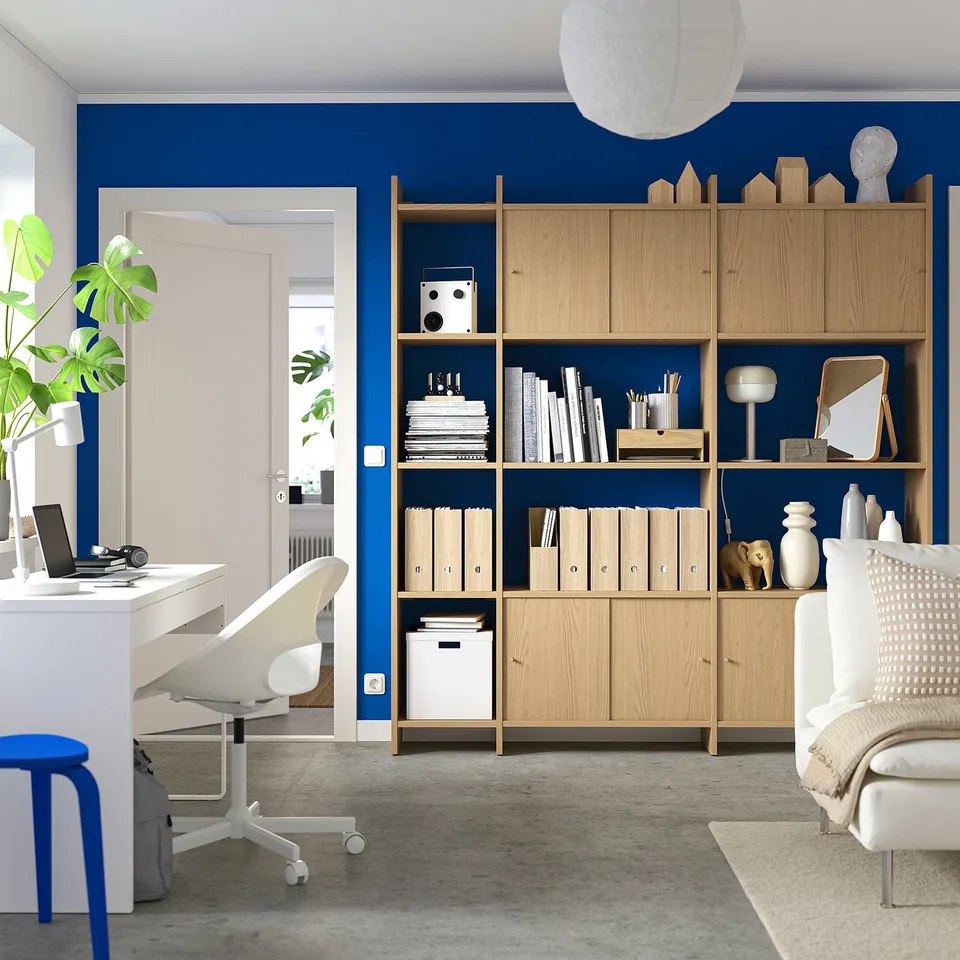 Modern home office with blue accent wall, light wooden shelves, white desk, and chair.