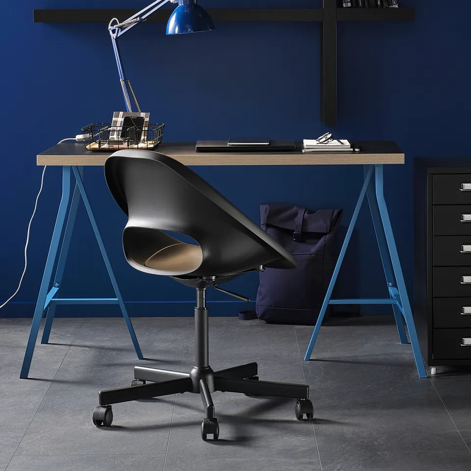 Modern blue office setup with ELDBERGET chair, blue lamp, and shelves against a dark blue wall.