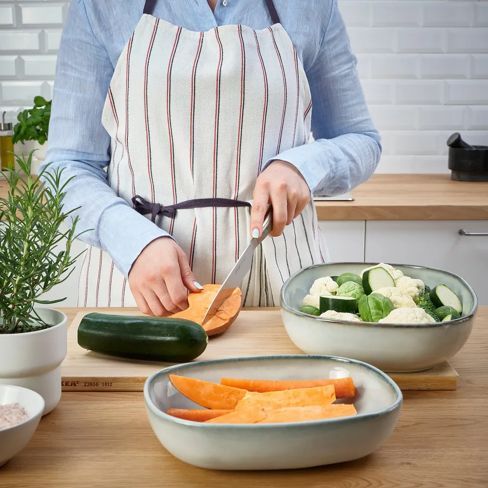Person slicing sweet potato in kitchen, using GLADELIG dish for prepared vegetables.