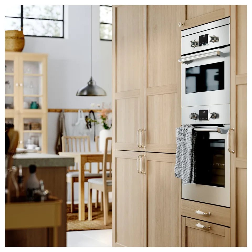 Modern kitchen with light wood cabinets, built-in oven, hanging light, chairs, and dining table.