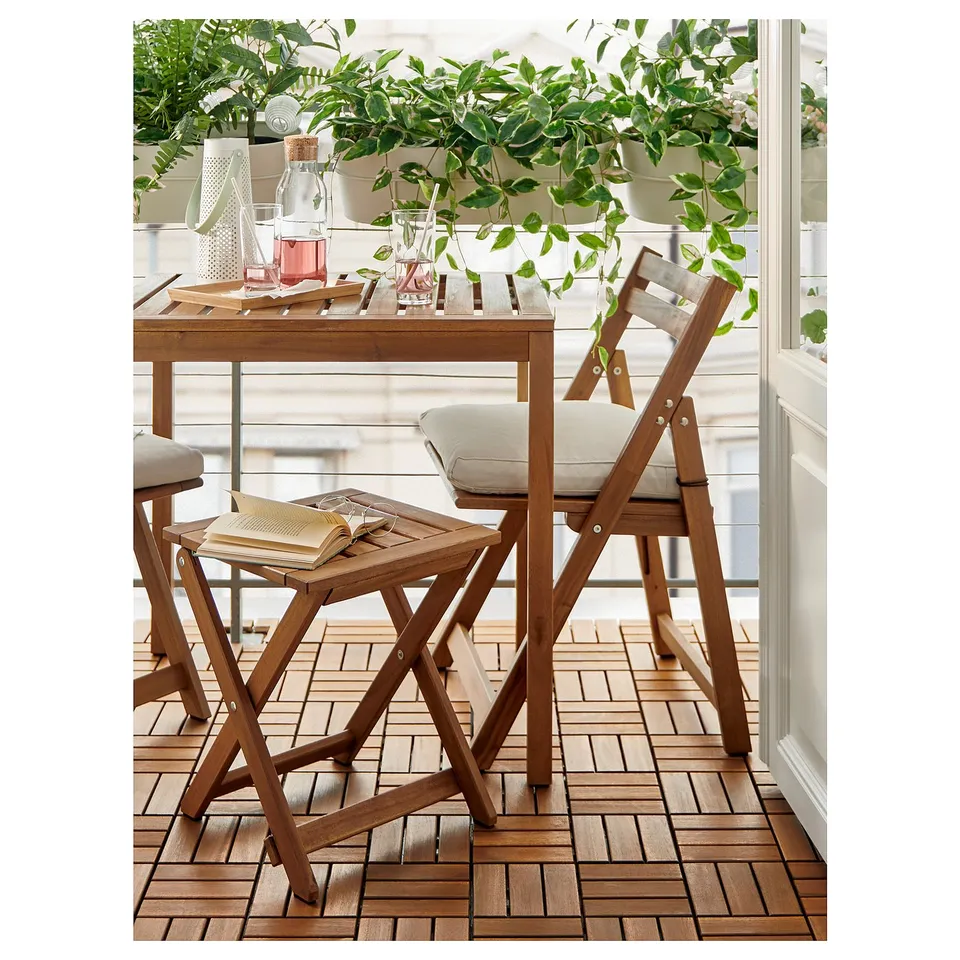 Cosy balcony scene with wooden NÄMMARÖ table and chairs, plants, and cushions.