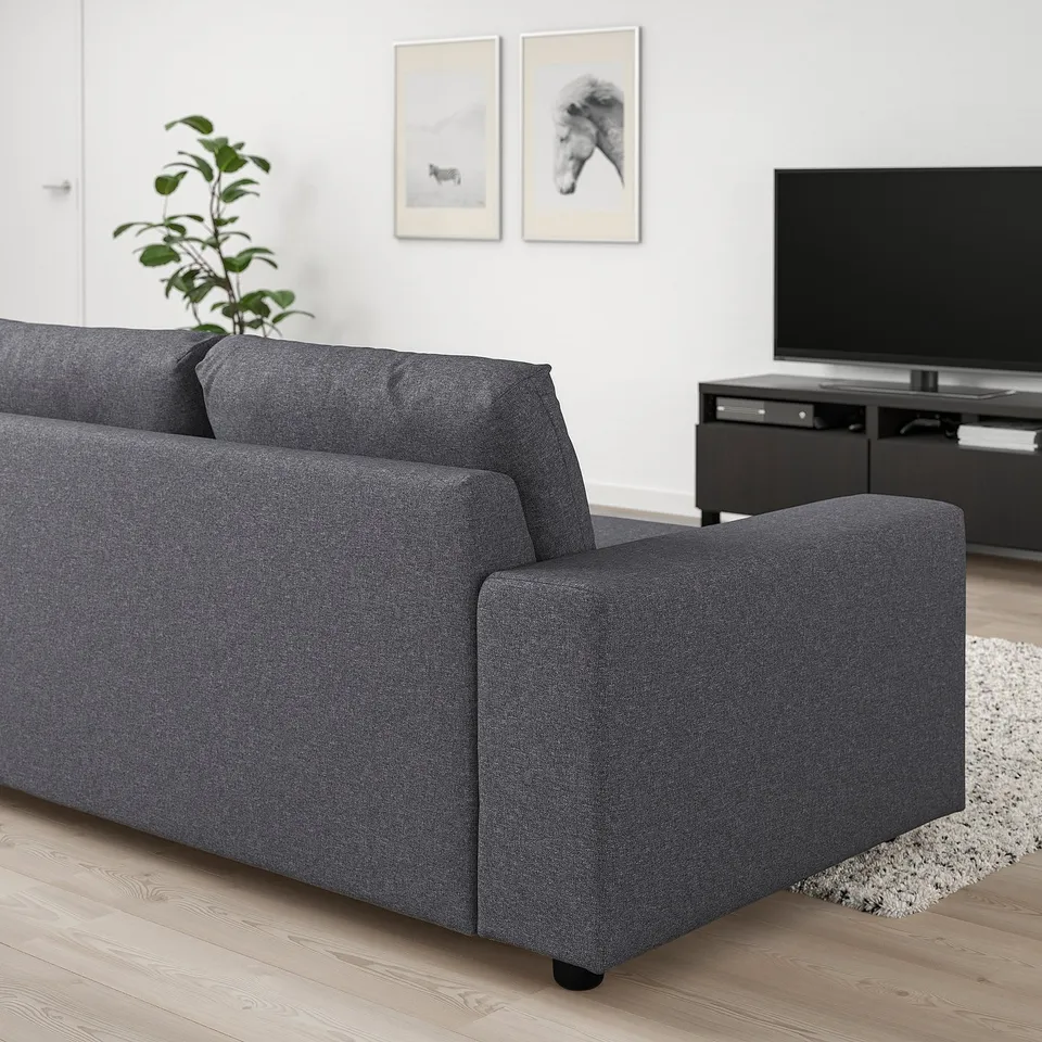 Modern black VIMLE sofa in living room, sleek and low-profile, facing tv with plant nearby.