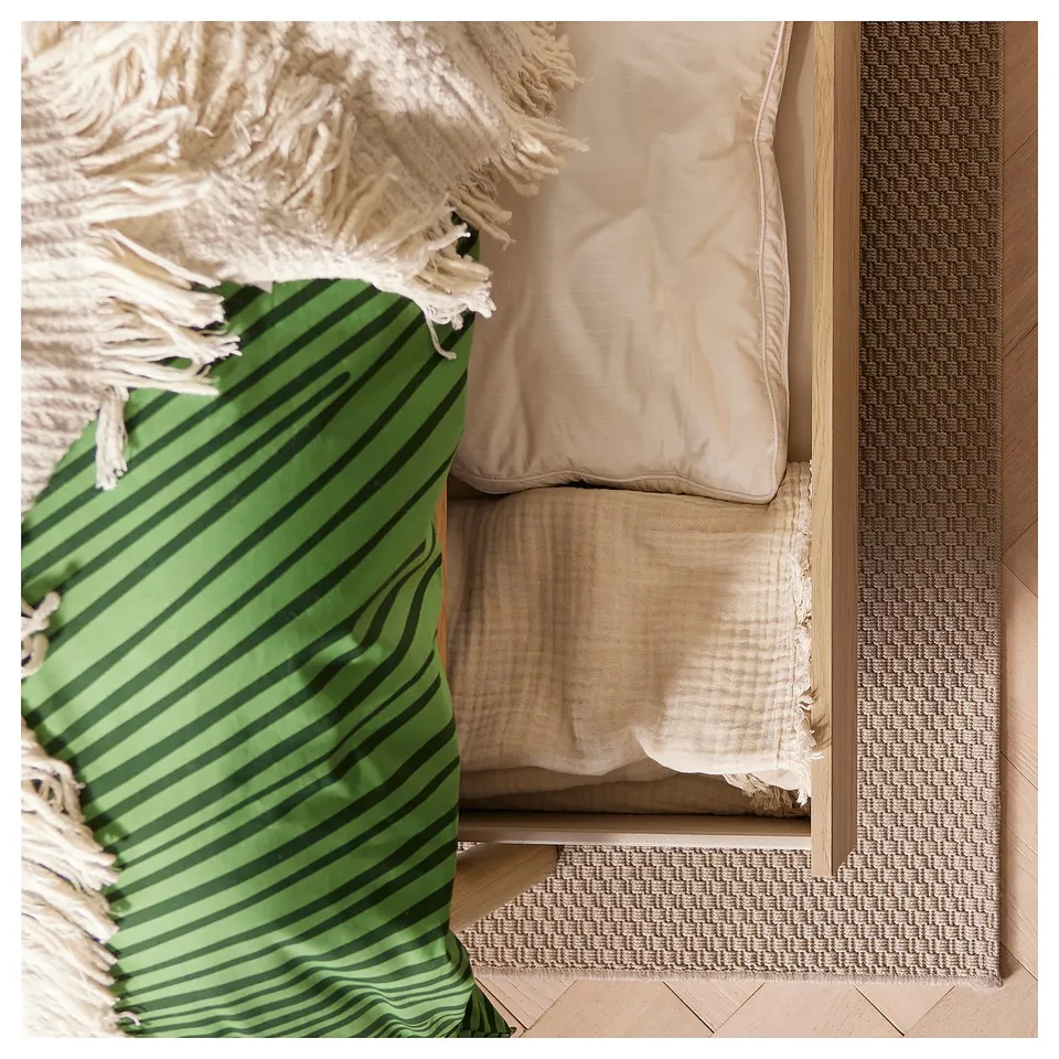 A green and beige striped rug next to a beige pillow on a wooden floor.