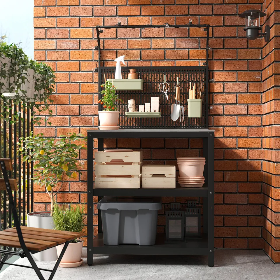Black metal outdoor kitchen with storage & hooks, against a brick wall.