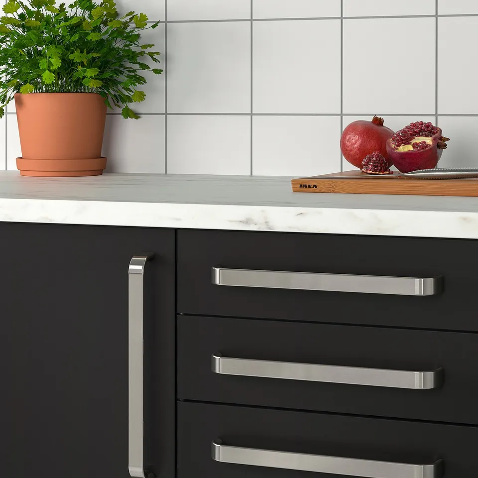Modern kitchen with black cabinets, stainless handles, white countertop, herb plant, and cut pomegranate.