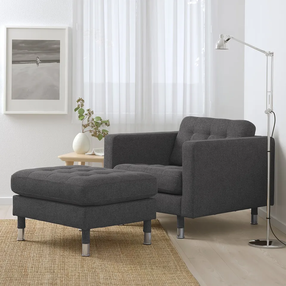 Minimalist living room with grey armchair, ottoman, lamp, and beach photo.