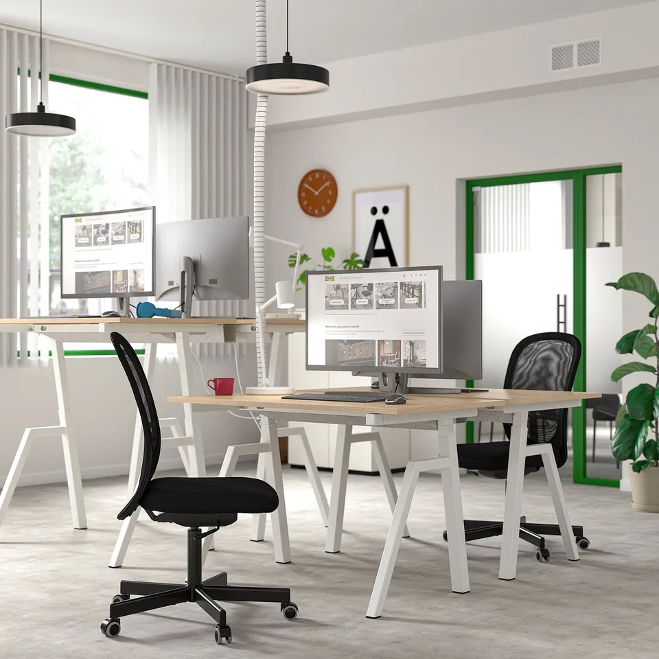 Modern TROTTEN sit/stand desks in ash and white with black/white chairs, computers, and plants in a minimalist workspace.