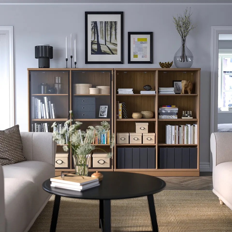 Grey living room with bookcase, sofas, and flower vase.