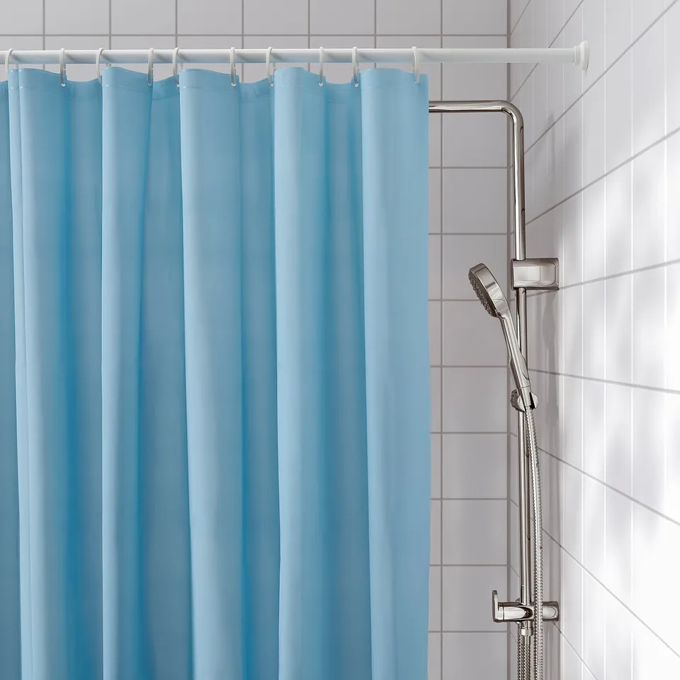 Light blue shower curtain on white rod, revealing silver shower head and hose on tiled wall.
