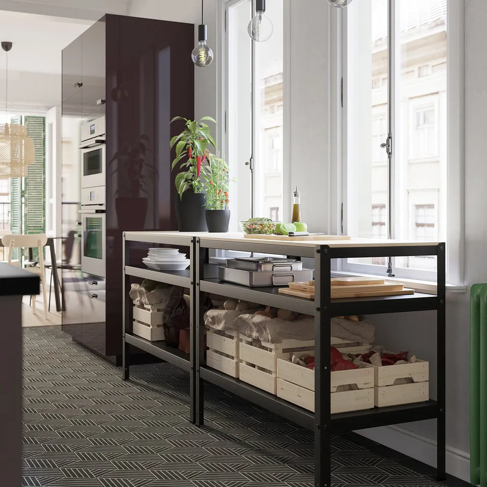 Modern open shelving unit in kitchen with potted plant and kitchenware. Black metal frame, light wood shelves.