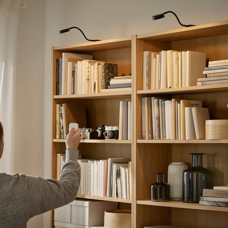 A person adjusts a bendable cabinet lamp, lighting books on shelves.