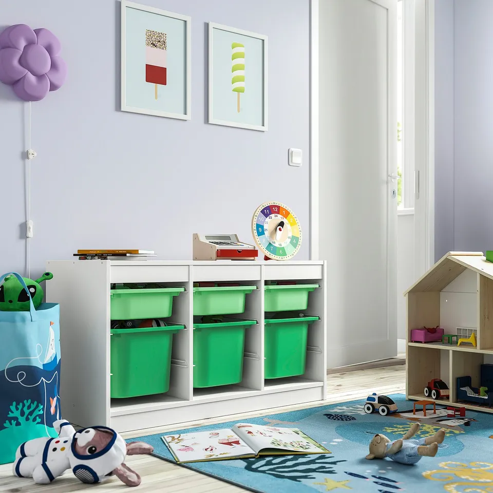 Kids room with white TROFAST storage unit, green bins, colourful art, toys, and books on blue rug.