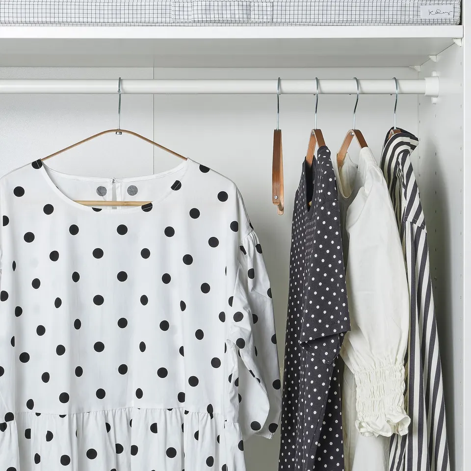 Closet with four hangers: one white polka dot dress, two dark polka dot blouses, one striped dress. Bamboo hangers keep clothes neat.