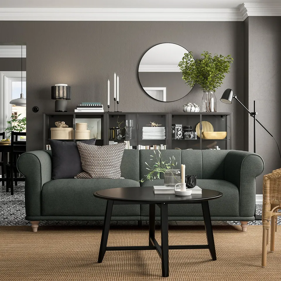 Modern living room with green VISKAFORS sofa, round black coffee table, grey walls, and dark wooden furniture.