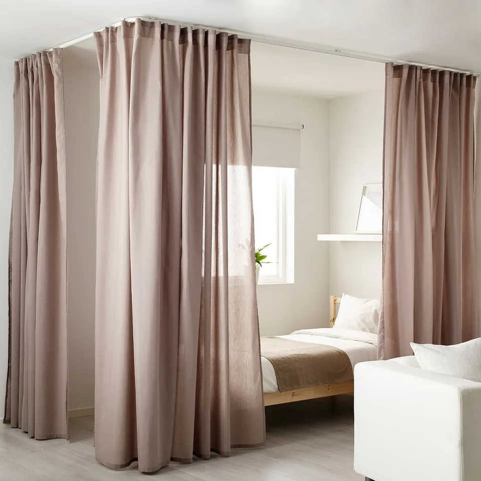Beige VIDGA curtains block light around corner bed. Plant on windowsill, minimalist room, bright.