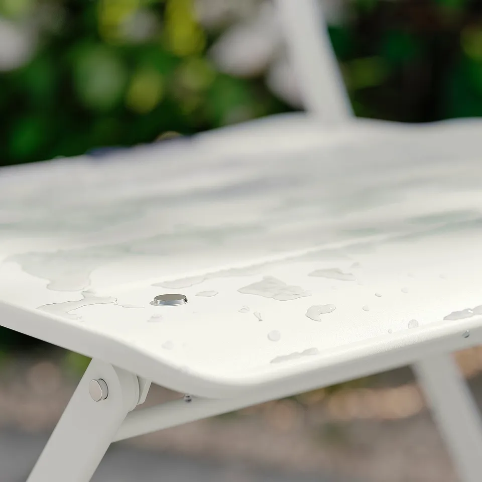 White metal outdoor table with water drops, partly folded, set outside.