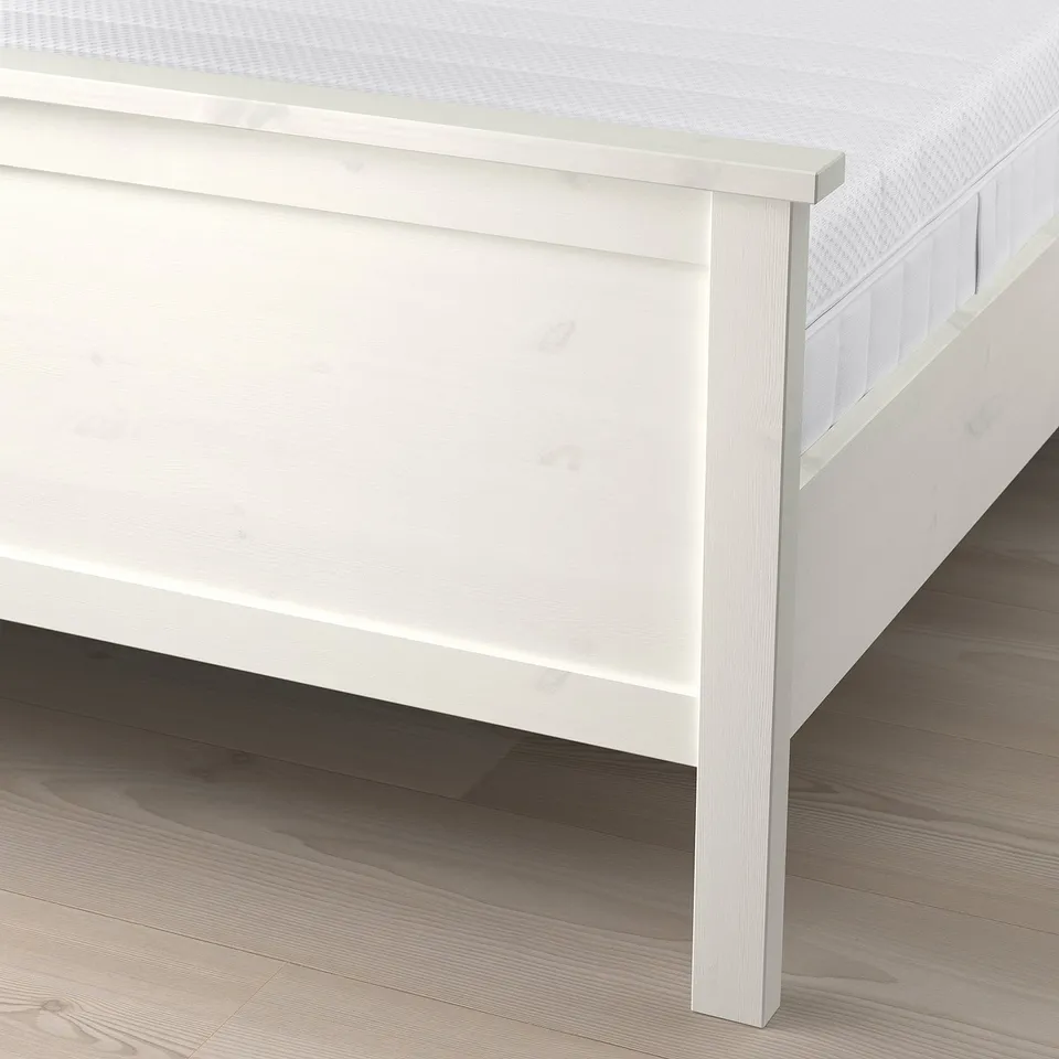 A white wooden bed frame with a high footboard, showing slats supporting a mattress, indicating durability and mattress compatibility.