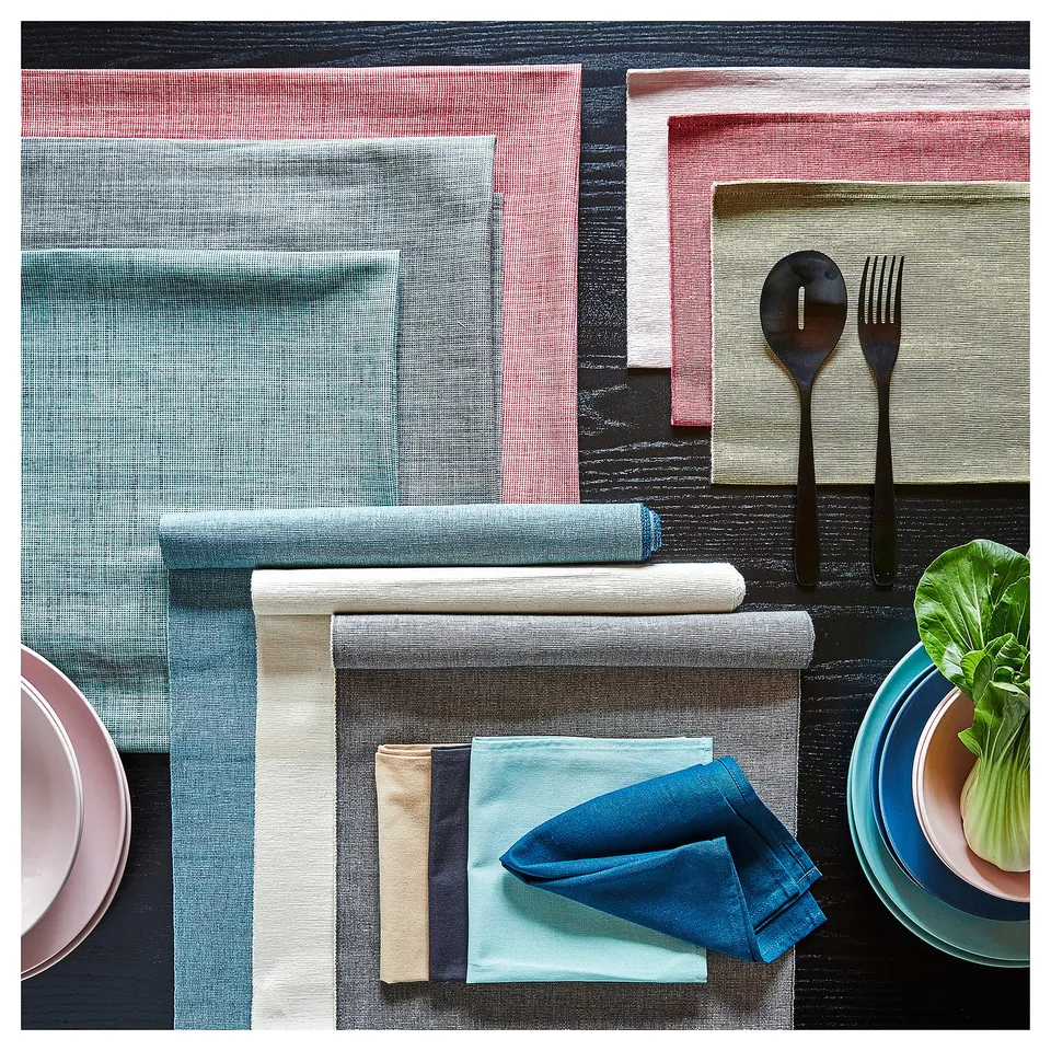 Black table setup with blue napkins, plates, and silverware on colourful mats.