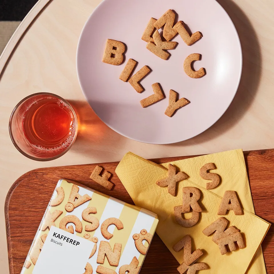 Alphabet cookies spell billy on pink plate, with yellow box and drink on wood table.