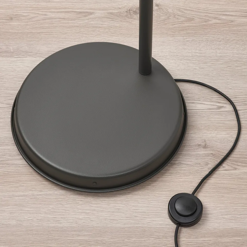 Round black floor lamp base with foot switch on wooden floor. High-quality finish and durable materials.
