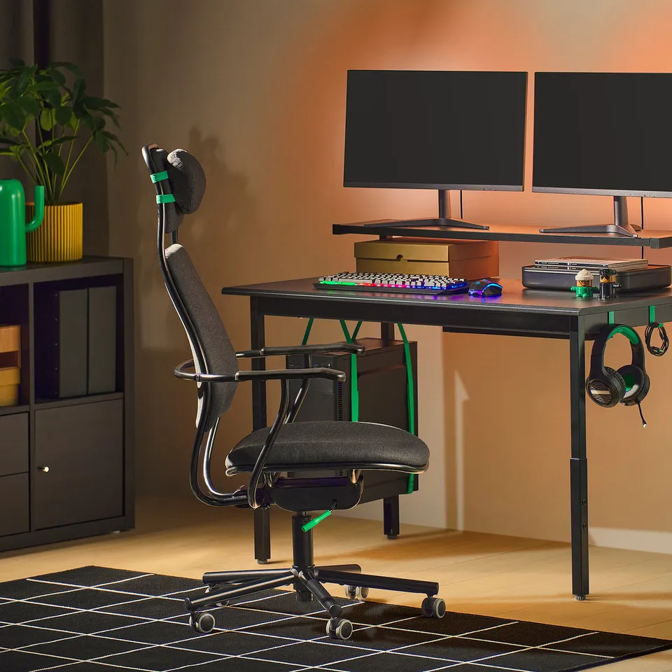 LÖPARBANA gaming chair, black with neon green, adjustable headrest, under black desk with dual monitors, on wheels.