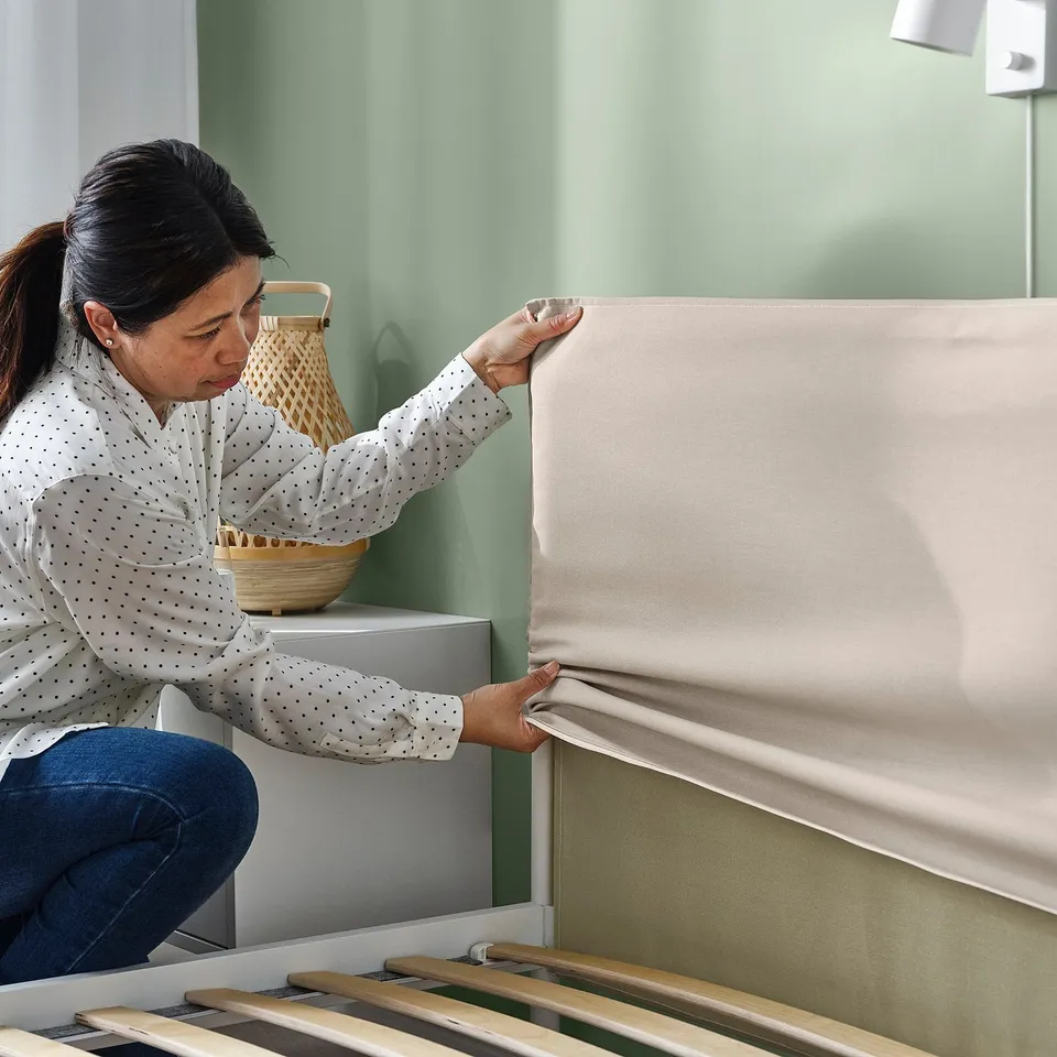 A person adjusts a KLEPPSTAD beds textile headboard, demonstrating its removable feature.