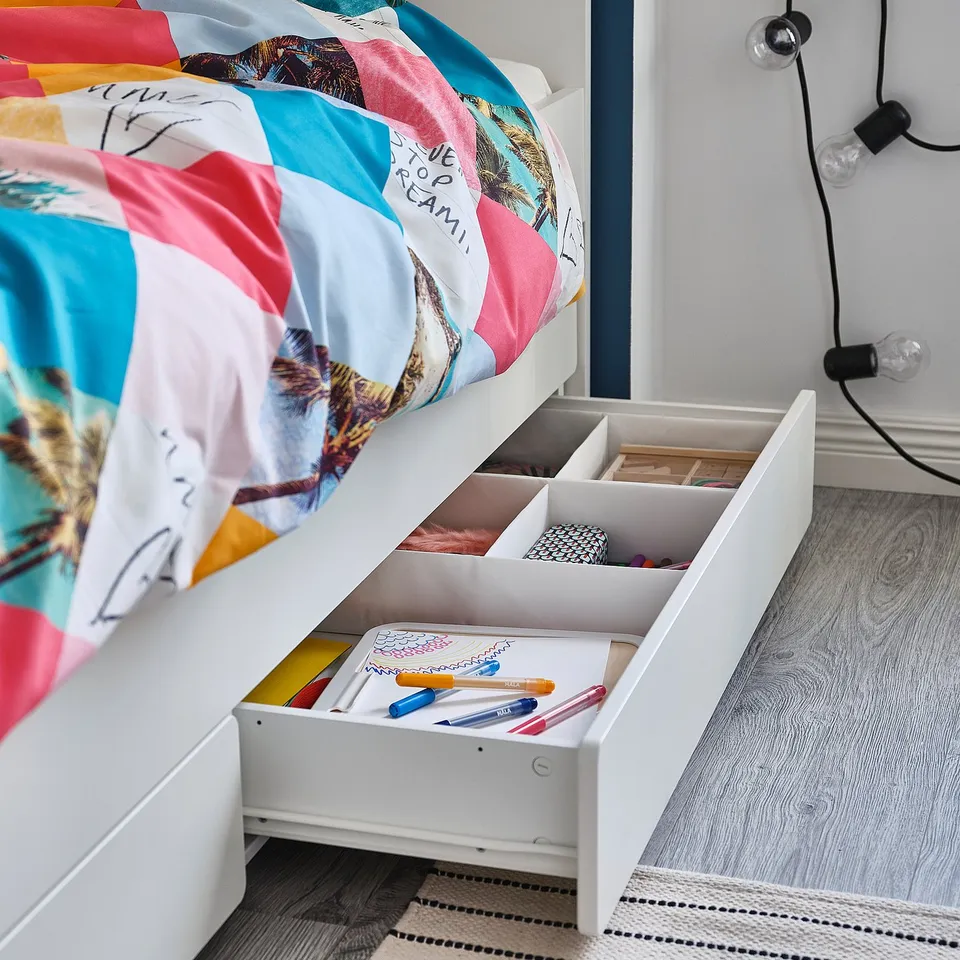 Bright, colourful bedspread with dream big on white bunk bed; drawers with pens and papers beneath.