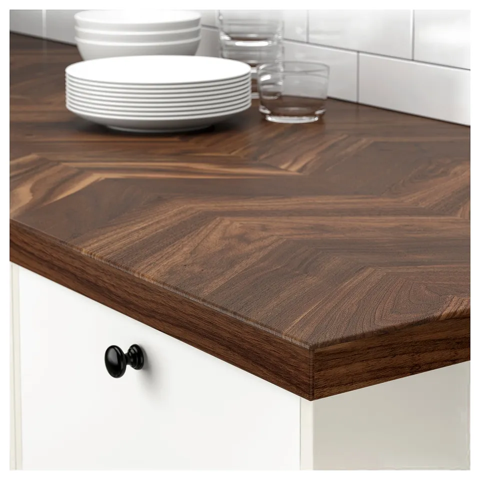 Dark brown wooden kitchen countertop with stacked plates and glasses, supported by white cabinets with black knobs.
