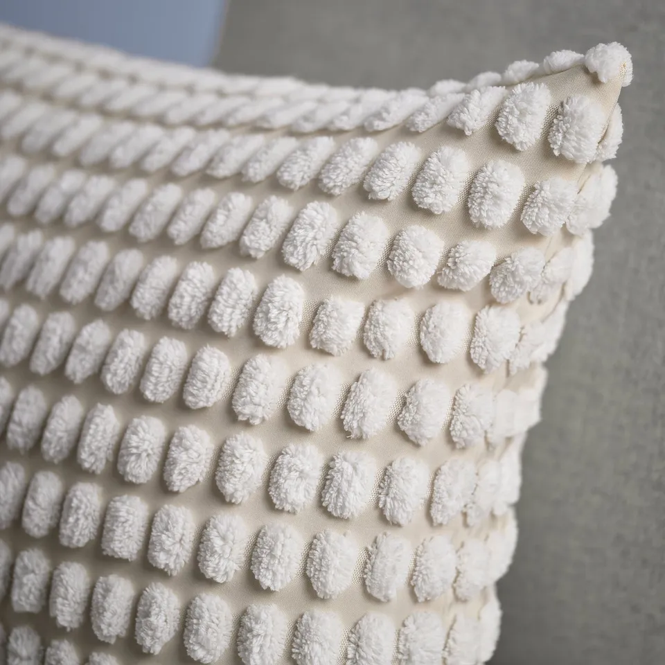 Close-up of a soft, white cushion cover with a textured, heart-shaped pattern and visible stitching detail.